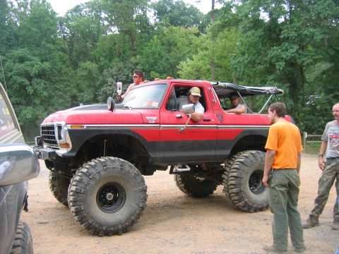 1992 Ford Mustang - A red lifted off-road vehicle with a black stripe and large tires is parked on a dirt road.