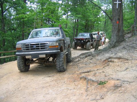 1992 Ford Mustang - A lifted 1992 Ford F-Series truck leads a line of off-road vehicles on a wooded trail.