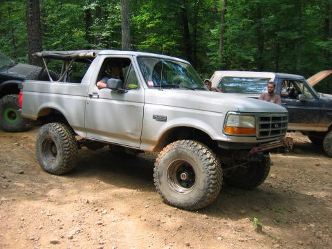 1992 Ford Mustang - A lifted Ford Bronco is parked on a dirt trail surrounded by trees, with other vehicles present.