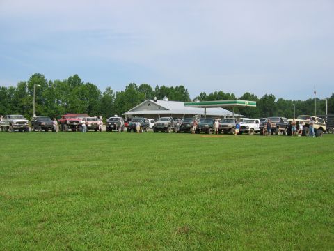 1992 Ford Mustang - A gathering of various off-road vehicles is parked on a wide, green lawn. Several people stand around the vehicles.