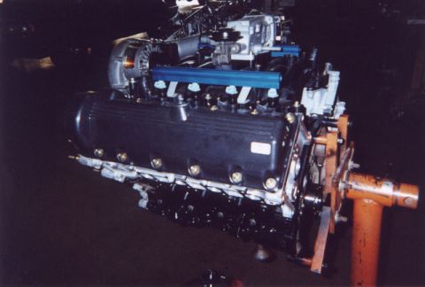1992 Ford Crown Victoria - A DOHC V8 engine mounted on an orange engine stand, with black valve covers, blue aluminum fuel rails, and a supercharger unit atop the int…