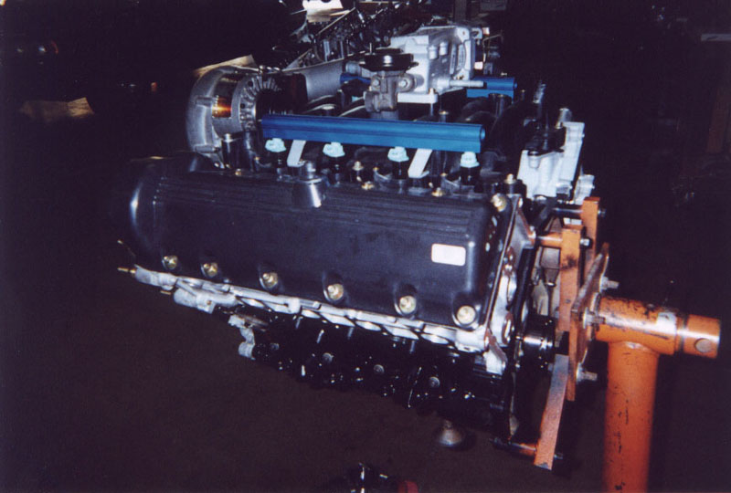 DOHC V8 with blue fuel rails and supercharger on an orange engine stand