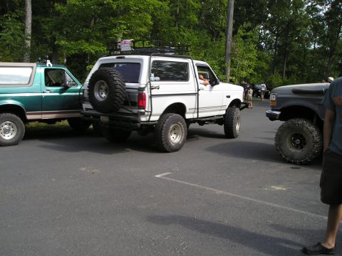 1996 Ford Bronco - Three off-road vehicles are parked in a lot with trees in the background.