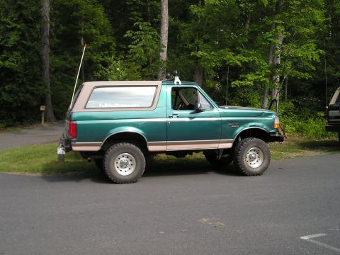 1996 Ford Bronco - A green 1996 Ford Bronco with tan trim is parked on asphalt with trees in the background.