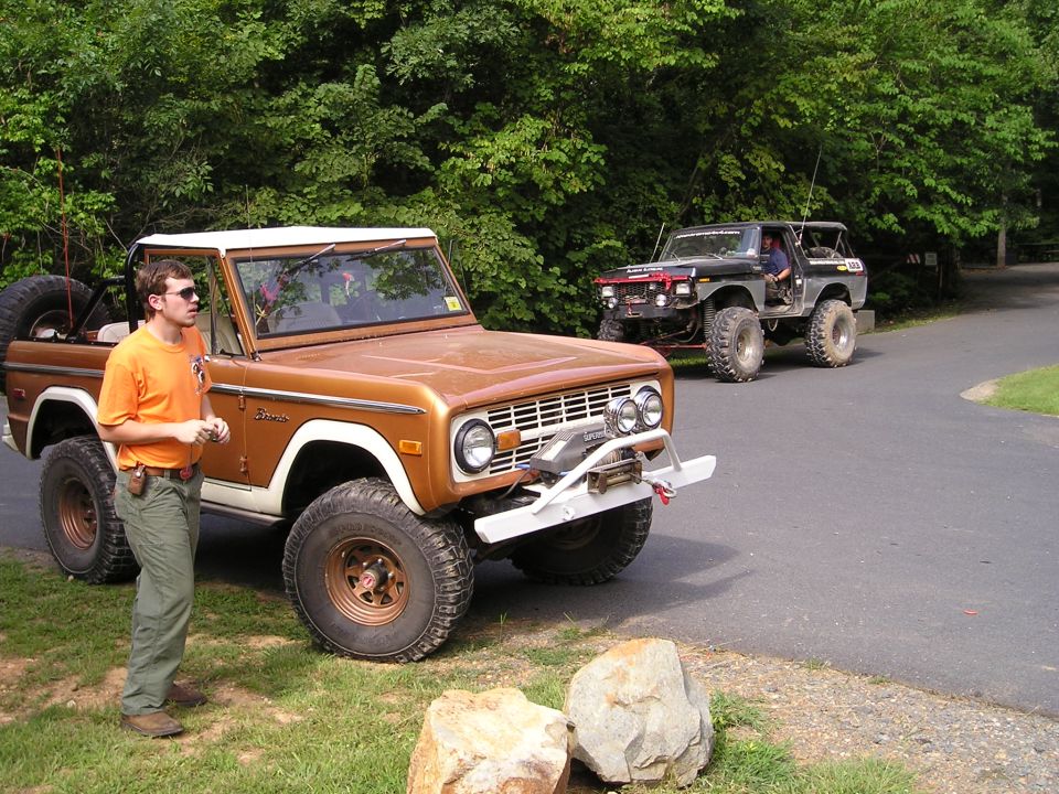 Bronze first-generation Ford Bronco with white roof, front winch, and spare tire on back. Second Bronco visible