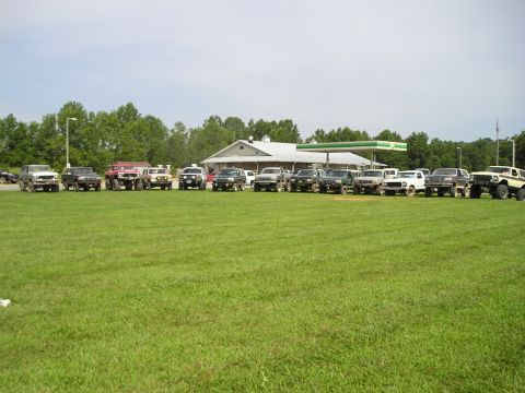 1996 Ford Bronco - Multiple SUVs and trucks are parked in a grassy field near a gas station.