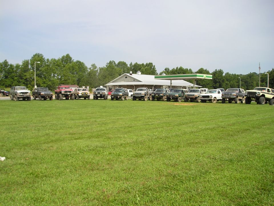 Line of SUVs and trucks parked on grass, gas station in background
