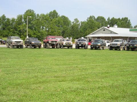 1996 Ford Bronco - A group of modified SUVs are parked on a lawn near a building.