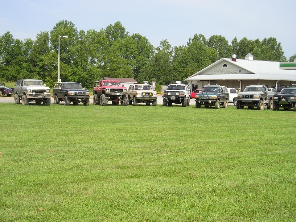 Several lifted SUVs parked in a row on grass in front of a building