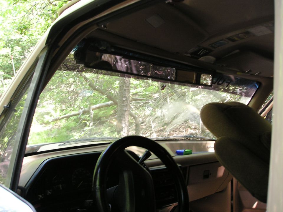 View from inside an old SUV, looking out the windshield at trees. Steering wheel and dashboard visible