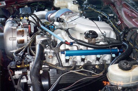 1992 Ford Crown Victoria - Close-up of a V8 engine bay showing polished intake manifold, blue anodized fuel rails with red and blue lines, black wiring harnesses, and…