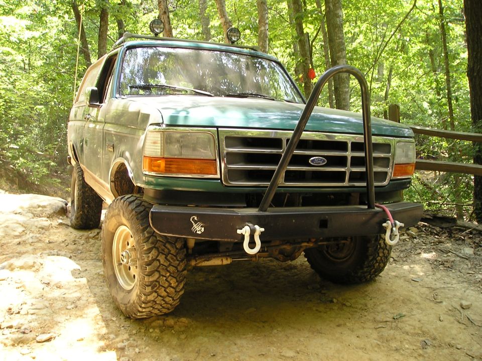 Green 1996 Ford Bronco with aftermarket front bumper and roll cage, parked on a dirt trail