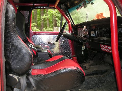 1996 Ford Bronco - The interior of this off-road vehicle features custom red and black seats, diamond plate accents, and a prominent roll cage.