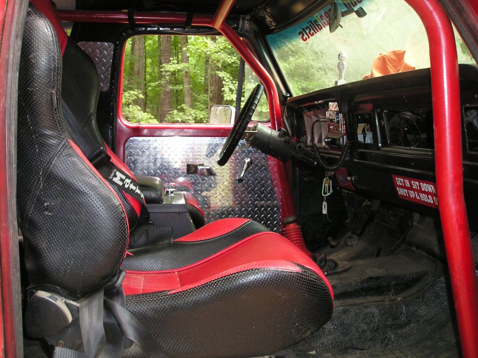 Interior of off-road vehicle with red and black seats, diamond plate door panels, and roll cage