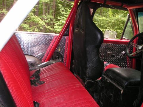1996 Ford Bronco - The interior of a modified off-road vehicle features red seats, a roll cage, and diamond plate accents.