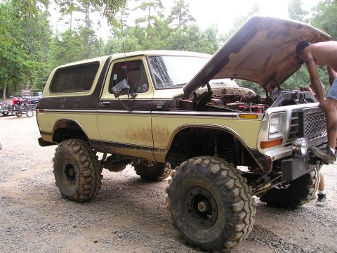 1996 Ford Bronco - A lifted Ford Bronco is being worked on with its hood open, while other vehicles and trailers are visible in the background.