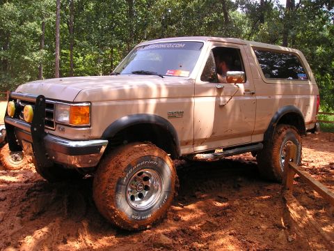 1996 Ford Bronco - This tan Ford Bronco navigates a muddy off-road course, its tires caked with dirt.