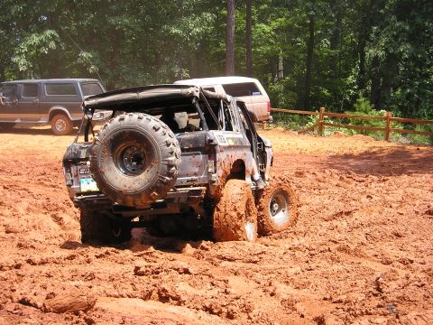 1996 Ford Bronco - This modified SUV is deep in the mud, with another vehicle parked nearby in a wooded area.
