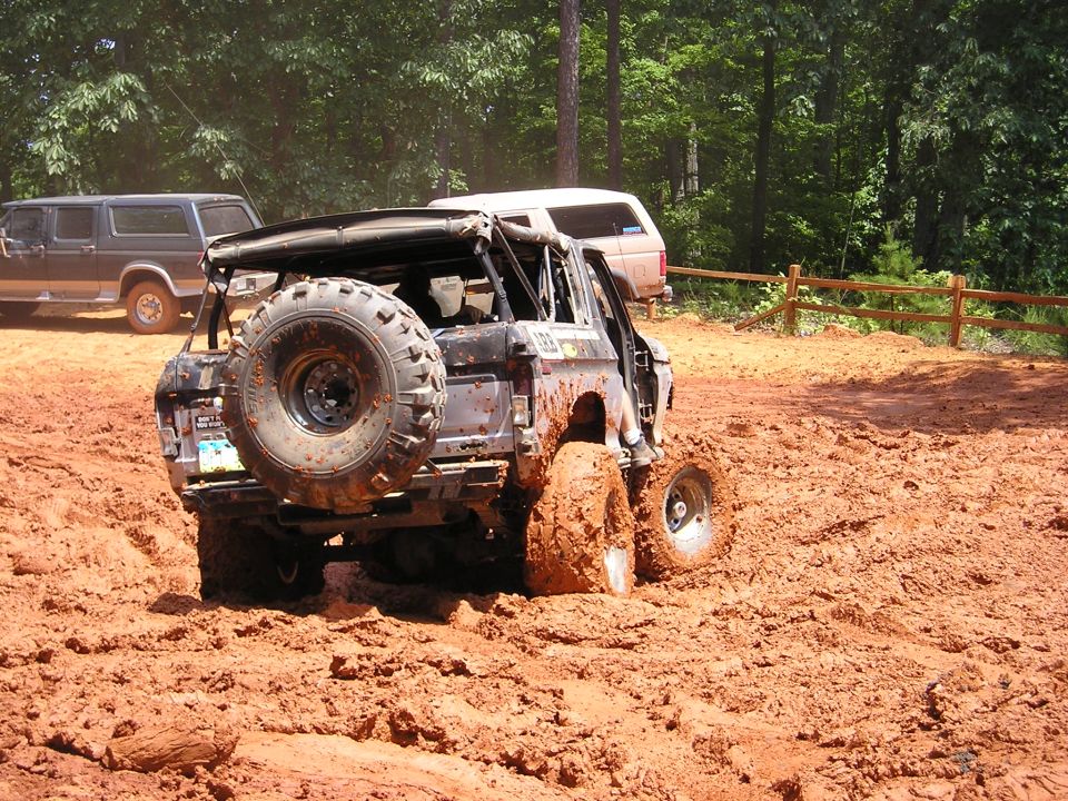 Muddy off-road SUV stuck in thick mud, with another SUV visible in the background