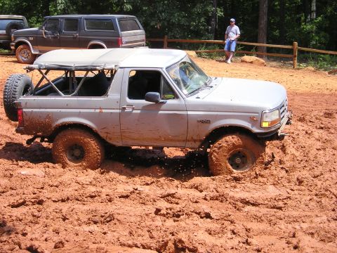 1996 Ford Bronco - This silver SUV navigates a challenging muddy terrain, with another vehicle and a bystander observing the off-road adventure.