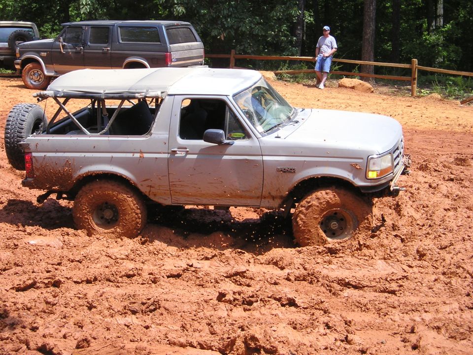 Silver SUV with soft top stuck in mud, side view. Another SUV and a man visible