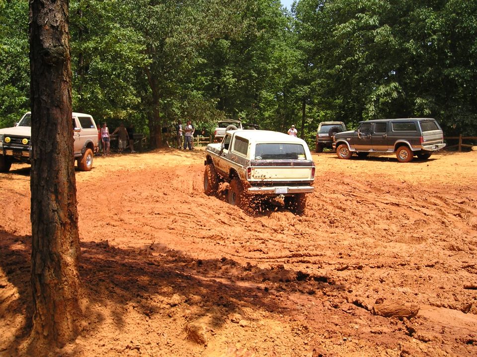 Tan Ford Bronco driving through mud, rear view. Mud splatters visible