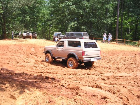 1996 Ford Bronco - Off-roading event with multiple SUVs and trucks tackling a challenging muddy terrain.