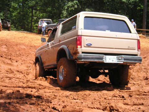 1996 Ford Bronco - A Ford Bronco navigates a muddy trail with other vehicles visible in the background.