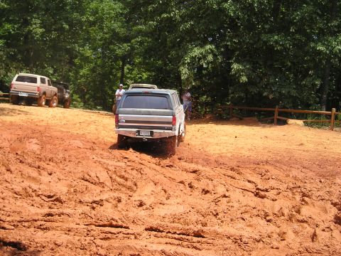 1996 Ford Bronco - A dark gray Ford Bronco navigates a muddy trail, with other off-road vehicles visible in the distance.