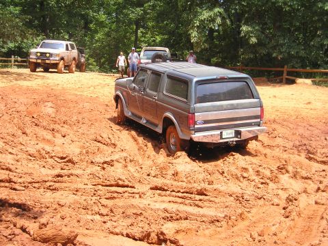 1996 Ford Bronco - A Ford Bronco navigates a muddy off-road trail with other vehicles and spectators present.