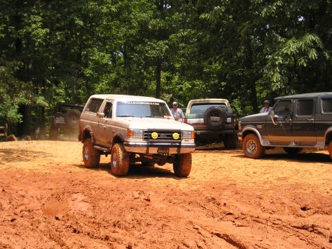 1996 Ford Bronco - Several Ford Broncos are seen off-roading on a muddy track surrounded by trees.