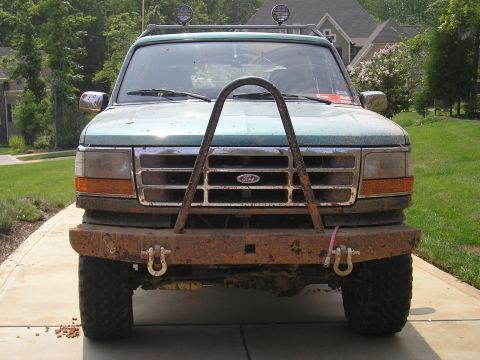1996 Ford Bronco - A green Ford truck with a custom bull bar and rusty bumper is parked on a driveway.