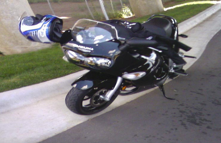 Black sport motorcycle parked at a curb with a blue and white helmet hanging on the left handlebar
