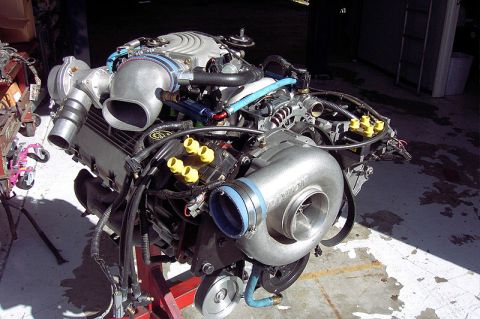 1992 Ford Crown Victoria - Fuel-injected V8 engine mounted on a red engine stand, fitted with a Paxton centrifugal supercharger with blue silicone couplers; yellow ca…
