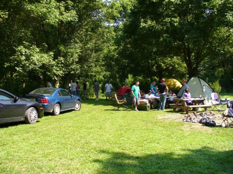 1991 Ford Probe - A blue coupe is parked on a grassy area with several people and tents set up in the background, suggesting an outdoor gathering or campsite.