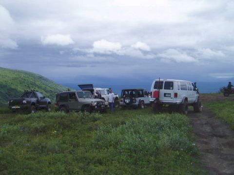 2000 Ford E350 - A group of off-road vehicles are gathered on a grassy hillside under a cloudy sky.