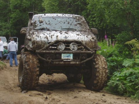 2000 Ford E350 - A heavily mud-splattered van is parked on a dirt path, with other vehicles and greenery in the background.