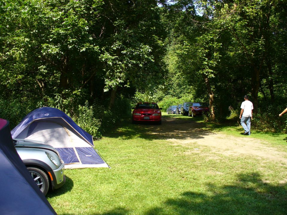 Red car parked on dirt road with tents and trees