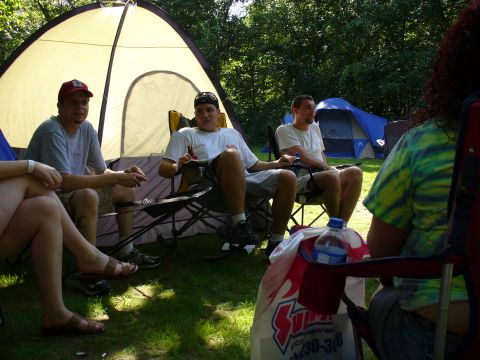 1991 Ford Probe - A group of people enjoy a camping trip, seated in chairs with tents set up behind them.