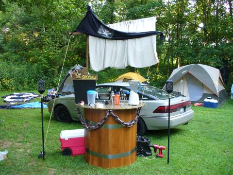 1991 Ford Probe - A silver hatchback serves as a makeshift bar at a campsite, complete with pirate-themed decorations and camping tents.