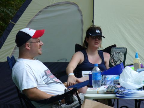 1991 Ford Probe - Two people are seated at a table near a tent, with various items including a fan and drinks on the table.