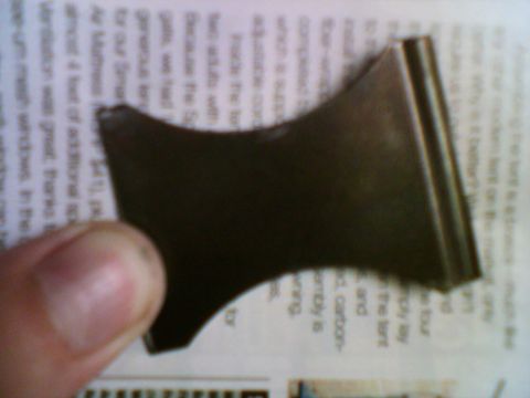 1985 Ford F-150 - A dark metal part is shown against a background of printed text on a newspaper.