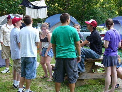 1991 Ford Probe - A group of friends relax at a campsite, with tents and trees surrounding them.