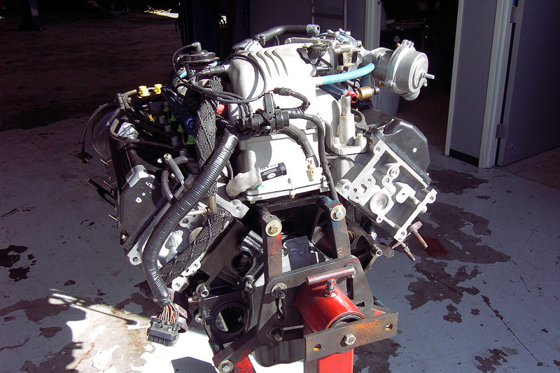 Supercharged Ford V8 engine assembled on a red engine stand outside a shop