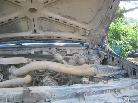 1990 Ford Bronco - The engine bay of a dusty vehicle is shown with the hood open, revealing various mechanical components.
