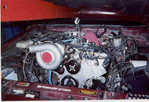 1992 Ford Crown Victoria - V8 engine being lowered into a red car's engine bay, hanging from a hoist with the serpentine belt, pulleys, white-taped intake tube and br…