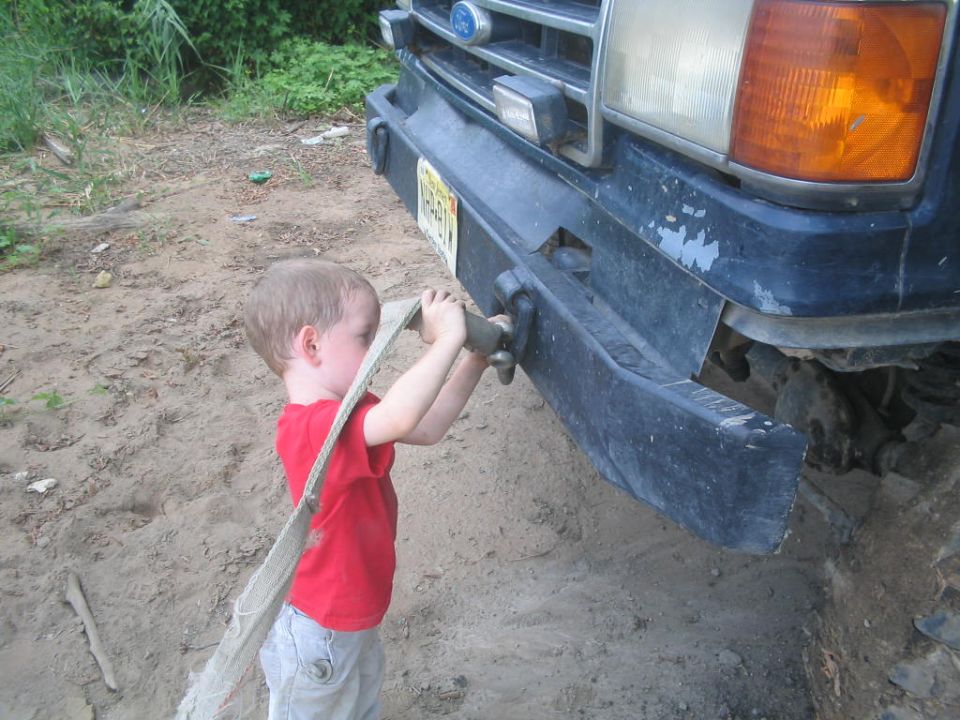 Child in red shirt holds tow strap attached to front bumper of 1990 Ford Bronco