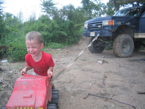 1990 Ford Bronco - A child pulls a toy truck while a 1990 Ford Bronco is attached by a strap.