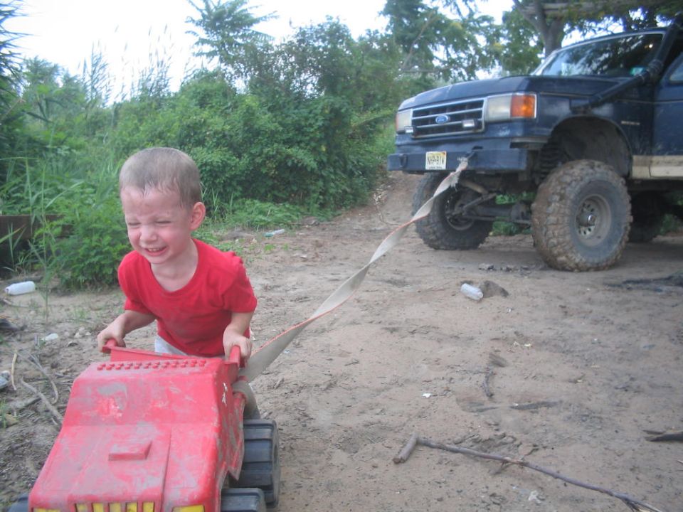 Blue 1990 Ford Bronco with large tires, front view, pulled by a child's toy