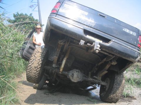 1990 Ford Bronco - A person stands by a black pickup truck that is stuck at an angle in a muddy, overgrown area.